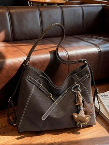 Large dark brown tote bag with white stitching and cute charms on a dark leather sofa