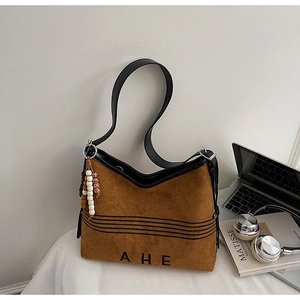 Detail of brown suede tote bag with beaded pendant and AHE logo in lifestyle setting