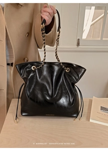 Detail of black faux leather tote with chain handle and brand logo on a wooden surface