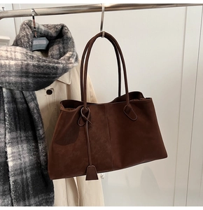 Detail of dark brown suede tote bag with long straps hanging in a minimalist autumn scene