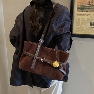 Detail of dark brown matte tote bag with leather buckle straps and flower charm