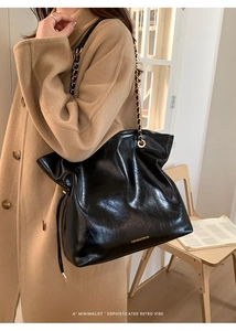 Détail d'un sac cabas en cuir noir avec bandoulière chaîne porté sur un manteau
