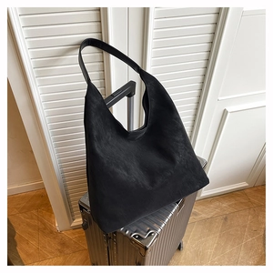 Detail of black suede tote bag with wide strap hanging on silver suitcase handle