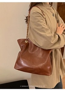Detail shot of the vintage brown leather tote bag with gold chain strap on an overcoat
