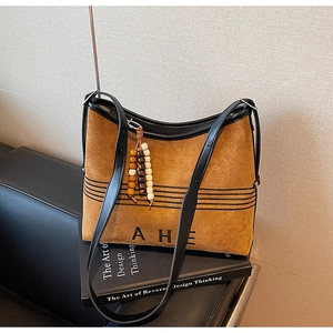 Detail of brown suede tote bag with black leather trim and decorative wooden bead charm