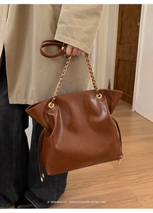 Close-up of retro brown leather tote bag detailing golden chain strap and side drawstring