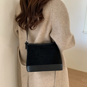 Detail of minimalist black patchwork tote bag worn over a khaki wool coat