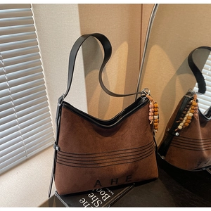 Close-up of brown suede tote bag with AHE embroidery and wooden bead tassel detail