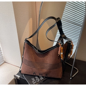 Close-up of brown suede tote bag with black letter embroidery and colorful wooden bead charm
