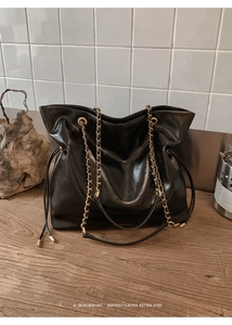 Detailed macro view of black glossy tote bag texture with metal chain and leather strap