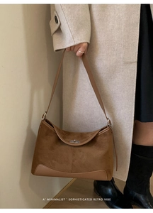 Detail view of brown matte suede shoulder bag with retro metal clasp on beige coat