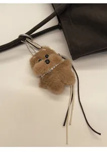 Detail of plush puppy bag charm with pearl necklace and engraved bone tag on a tote bag
