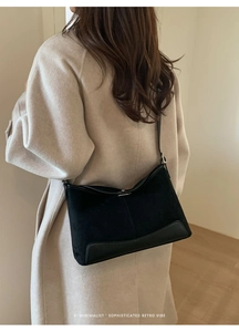 Detail of a minimalist black suede and leather crossbody bag on a beige wool coat