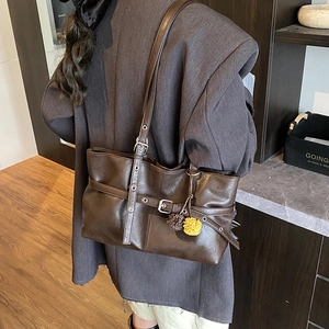 Brown faux leather tote bag with plush charms shown being worn by a model in a retro room