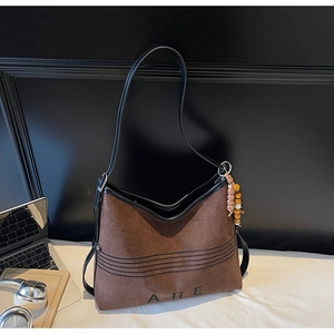 Close-up of brown suede tote bag with black leather trim and ethnic bead charm detail