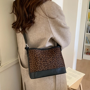 Detail of a leopard print shoulder bag with black leather stitching and adjustable strap