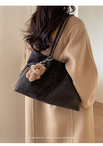 Brown frosted tote bag with a small plush dog charm worn by a model in a wool coat