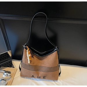 Detail of a brown suede tote bag featuring black piping and a colorful beaded tassel