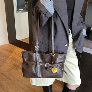Detail of dark brown leather tote bag with stylish plush ball charm and long shoulder strap