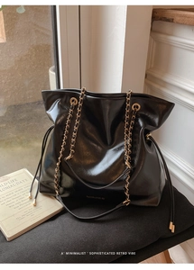 Detail of glossy black leather tote bag featuring gold chain strap and drawstring design
