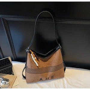 Detail shot of brown suede tote bag featuring black AHE logo and wooden bead charm