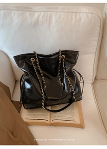 Detail of black glossy leather tote bag with gold chain strap and elegant brand logo