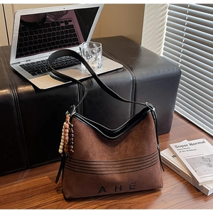 Macro detail of brown suede tote bag featuring AHE lettering and beaded tassel charm