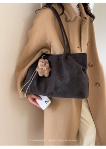 Detail of dark grey frosted leather tote bag with vertical stitching and bear charm