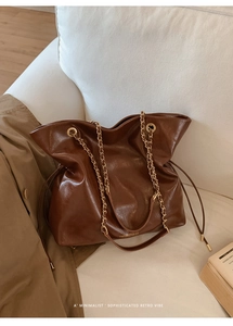 Detail of dark brown leather tote with chain strap and drawstrings on a white sofa