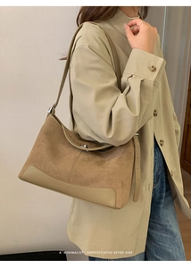 Detail of camel suede tote bag with silver metallic clasp worn by a model in a trench coat