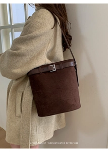 Détail d'un sac seau rétro en daim marron porté avec un manteau beige élégant et moderne