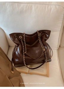 Detail of vintage dark brown tote bag with gold chain strap on a soft white sofa