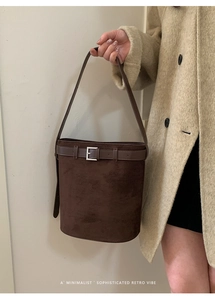 Détail du sac seau rétro en daim marron foncé avec boucle argentée sur un manteau