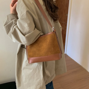 Detailed side view of a brown patchwork suede hobo bag styled with a khaki trench coat