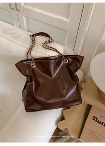 Detail of dark brown leather tote bag with gold chain strap on a white sofa setting