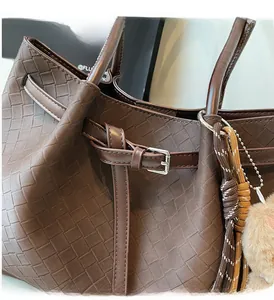 Detail of dark brown leather woven tote bag featuring silver buckle and plush charm