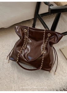 Detail of dark brown glossy leather tote bag with gold chain strap on white carpet