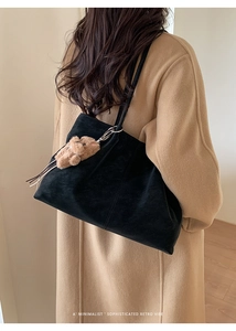 Detail shot of a black frosted tote bag on a camel coat with a cute bear charm pendant