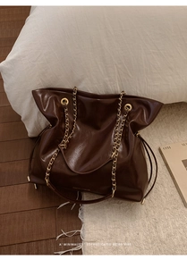 Detailed macro view of dark brown patent leather tote bag with gold chain and drawstring