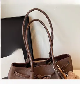 Detail of brown woven tote bag with slim round handles and a cute plush bear pendant