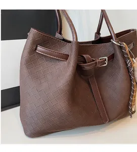 Close-up of brown woven faux leather tote bag with decorative silver buckle and charms