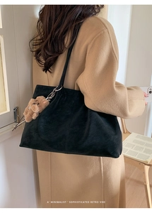 Detail of black frosted suede tote bag with brown plush bear charm on model in tan coat