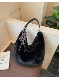 Detail of black faux fur hobo bag with leather handle and branded pendant on wooden stand