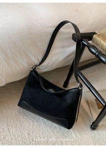 Close-up of minimalist black suede and leather shoulder bag with silver buckle detail
