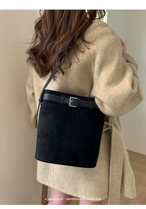 Détail du sac seau en daim noir avec boucle en métal argenté et design de bandoulière