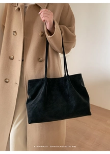 Minimalist large black matte tote bag with slim straps worn over a camel coat