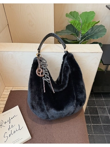 Detail of black faux fur hobo bag with leather handle and large decorative letter charm