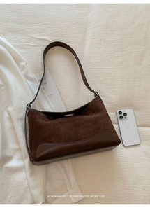 Close-up of brown suede underarm bag with vertical stitching and smooth leather accents