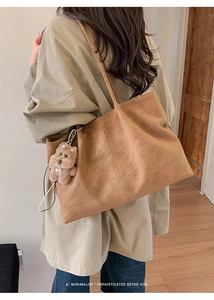 Detail of dark brown matte faux leather tote bag with vertical stitching and bear charm