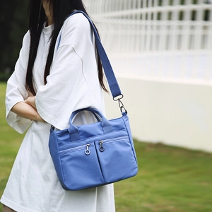 Blue nylon crossbody tote bag with dual front zippers worn by a model in outdoor setting